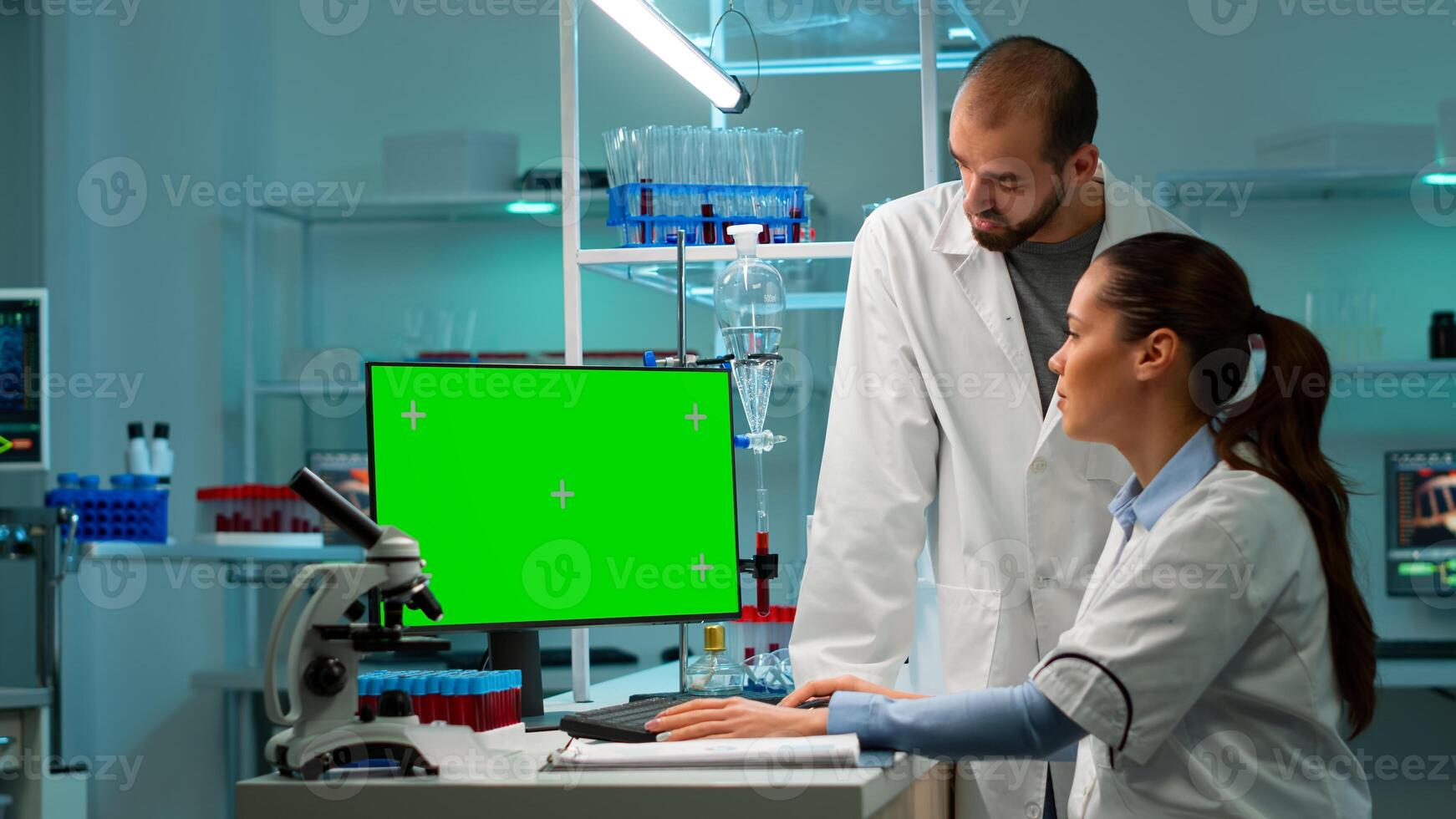 Modern medical research laboratory with two scientists using computer with green chroma key screen. Doctors specialists discussing innovative treatment, advanced scientific lab for medicine. photo
