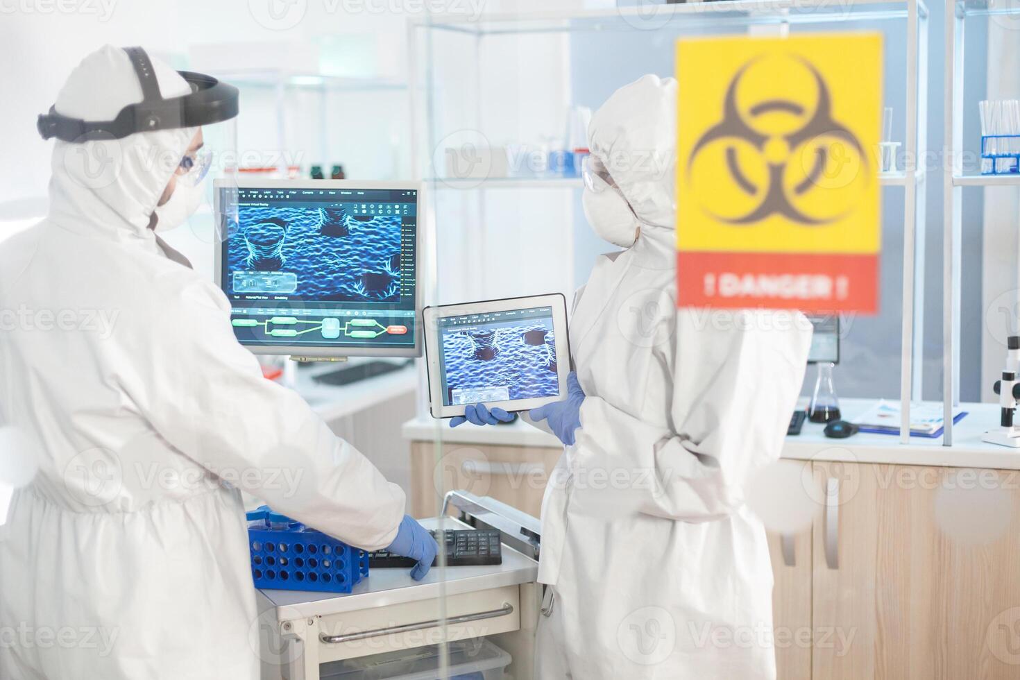 Scientist in laboratory danger zone using tablet pc dressed in ppe suit. Group of doctors examining vaccine evolution using high tech for diagnosis against covid19. photo