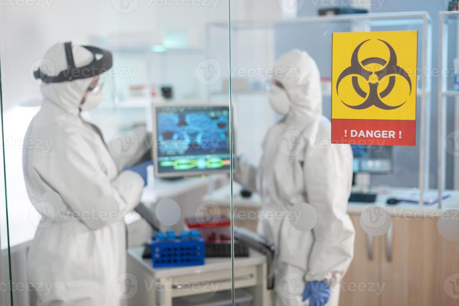 Danger zone sign in medical laboratory and scientist working dressed in ppe suit. Group of doctors examining vaccine evolution using high tech for diagnosis against covid19. photo