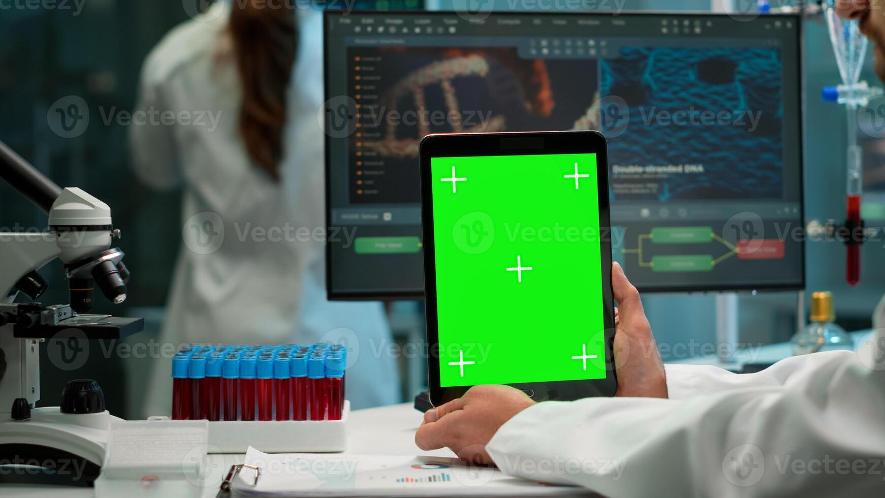 Male chemist scientist holding green mock-up screen tablet sitting at desk. In background technology research, development laboratory with specialist doctor working in high tech design photo