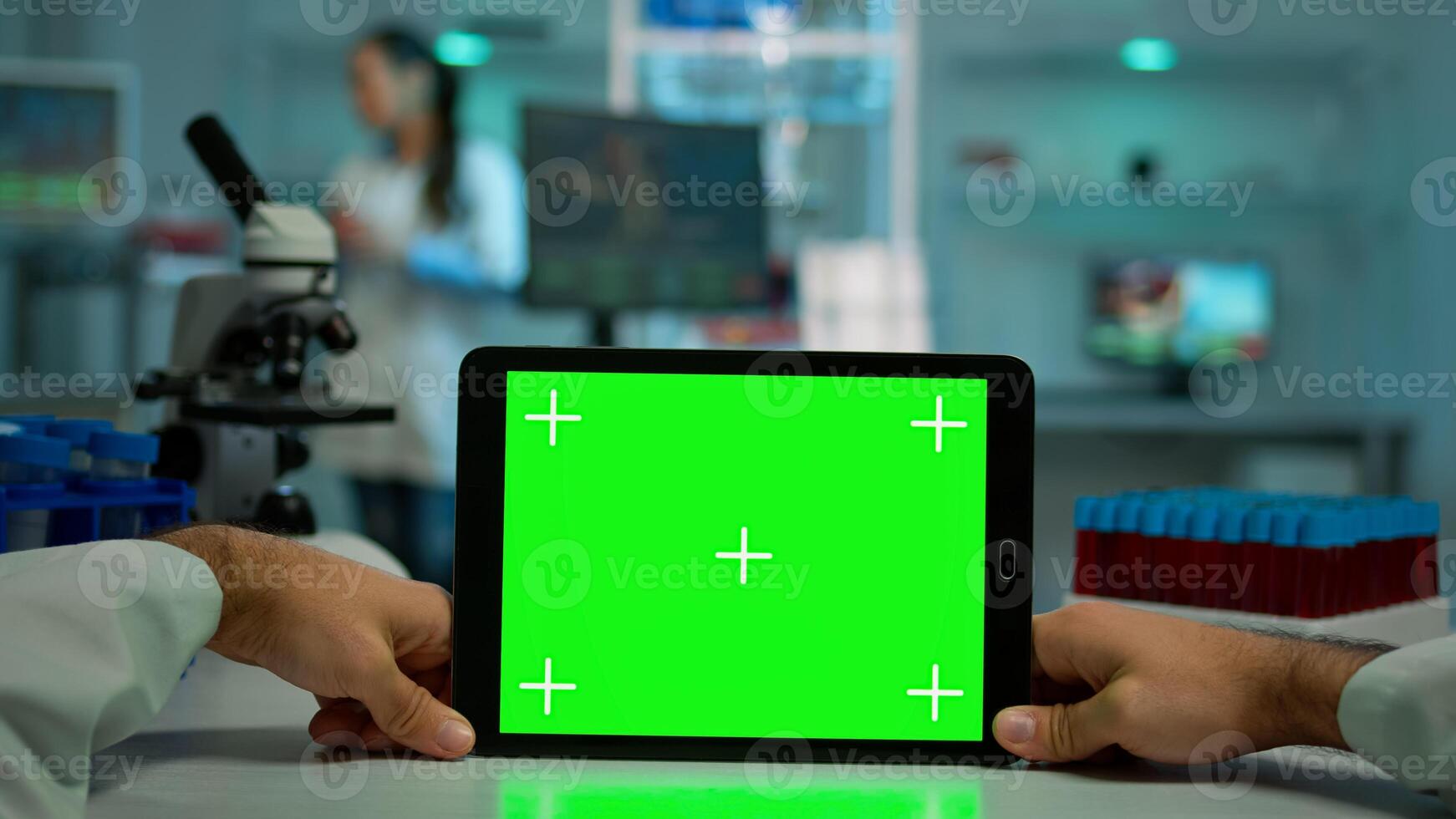 Pov shot of microbiologist holding tablet with green chroma key display sitting at desk working reading virus symptoms. In background lab researcher analysing vaccine developent examining samples photo