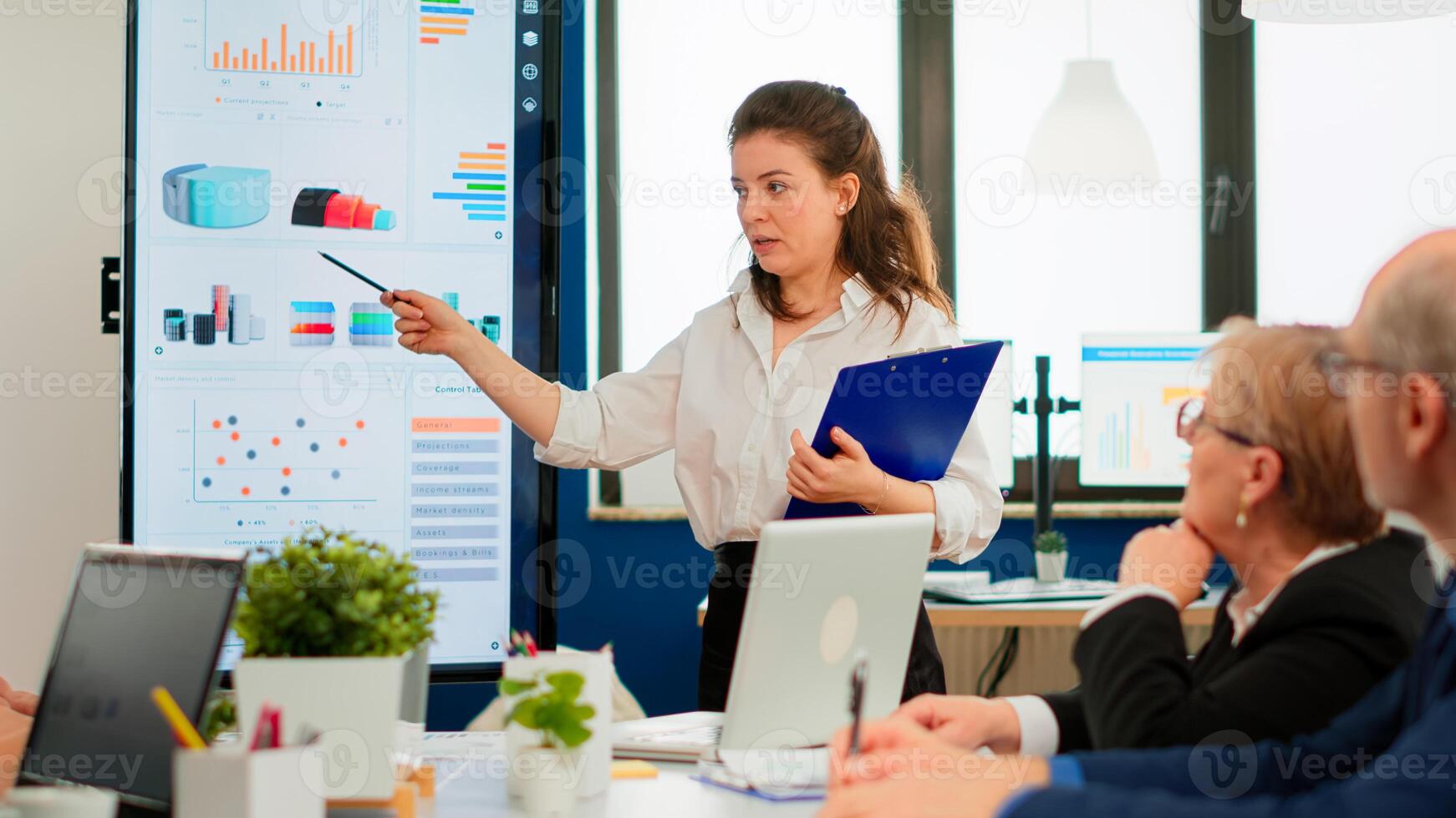 Young businesswoman coach leader conference speaker giving business presentation explain project strategy pointing on digital board training diverse team group at office boardroom seminar meeting photo