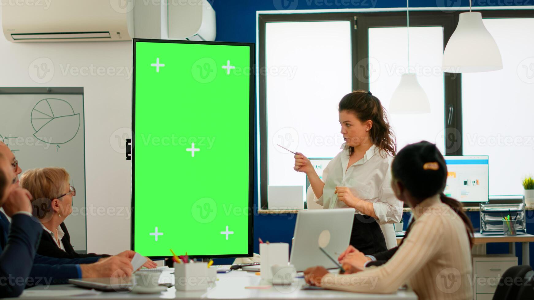 Young leader briefing diverse businessteam standing in front of meeting table analysing financial statistics, looking at greenscreen display. Multiethnic workers planning project on chroma key desktop photo