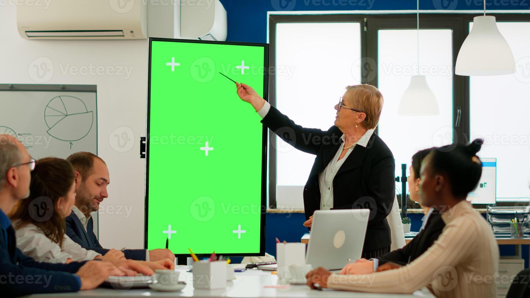 Diverse business team sitting at meeting table analysing financial statistics, looking at green screen display while senior leader explaning. Multiethnic workers planning project on chroma key desktop photo