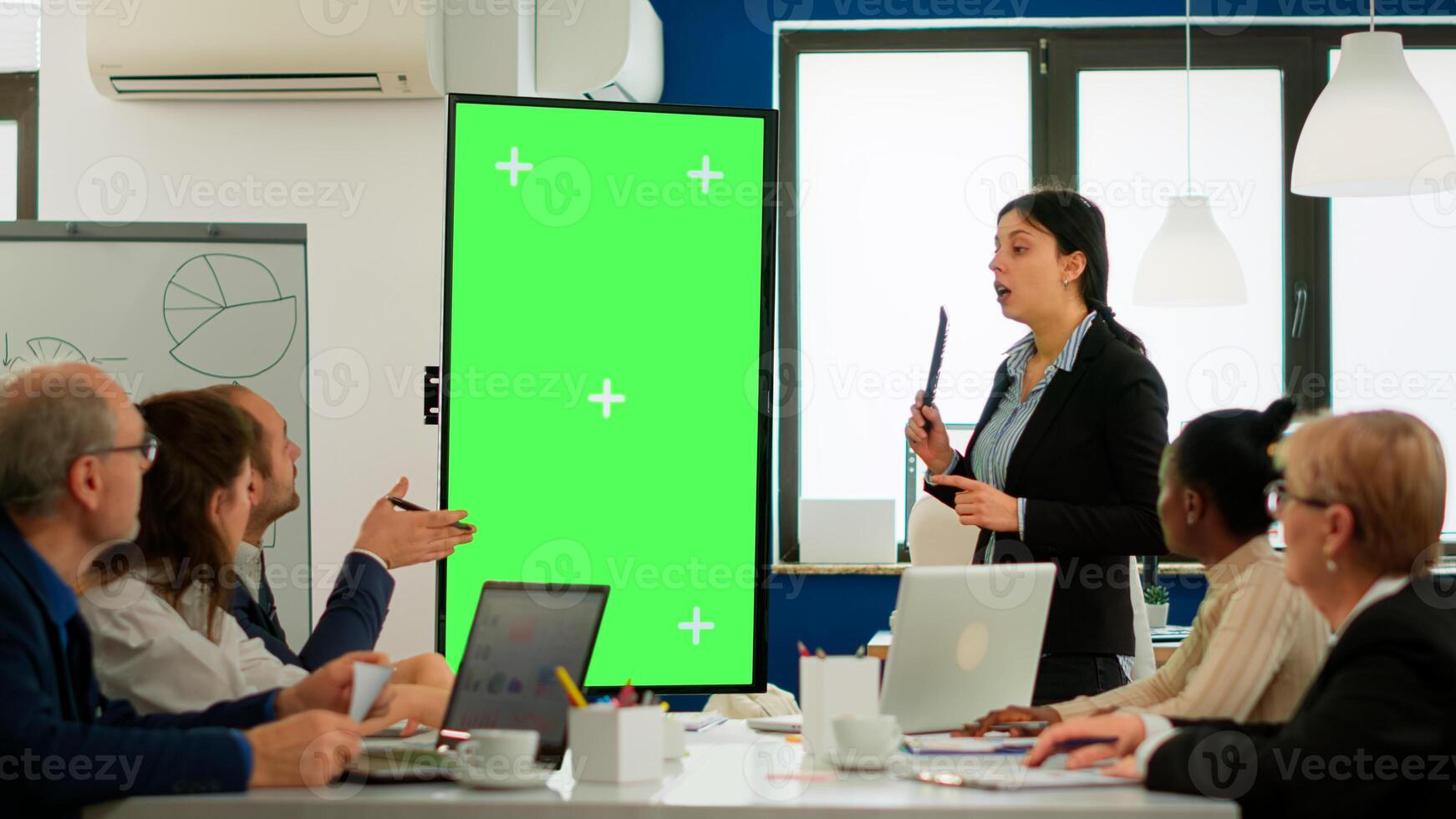 Leader of company presenting financial plan using mockup display in front of diverse team brainstorming. Manager explainig project strategy on green screen monitor with chroma key desktop in boardroom photo