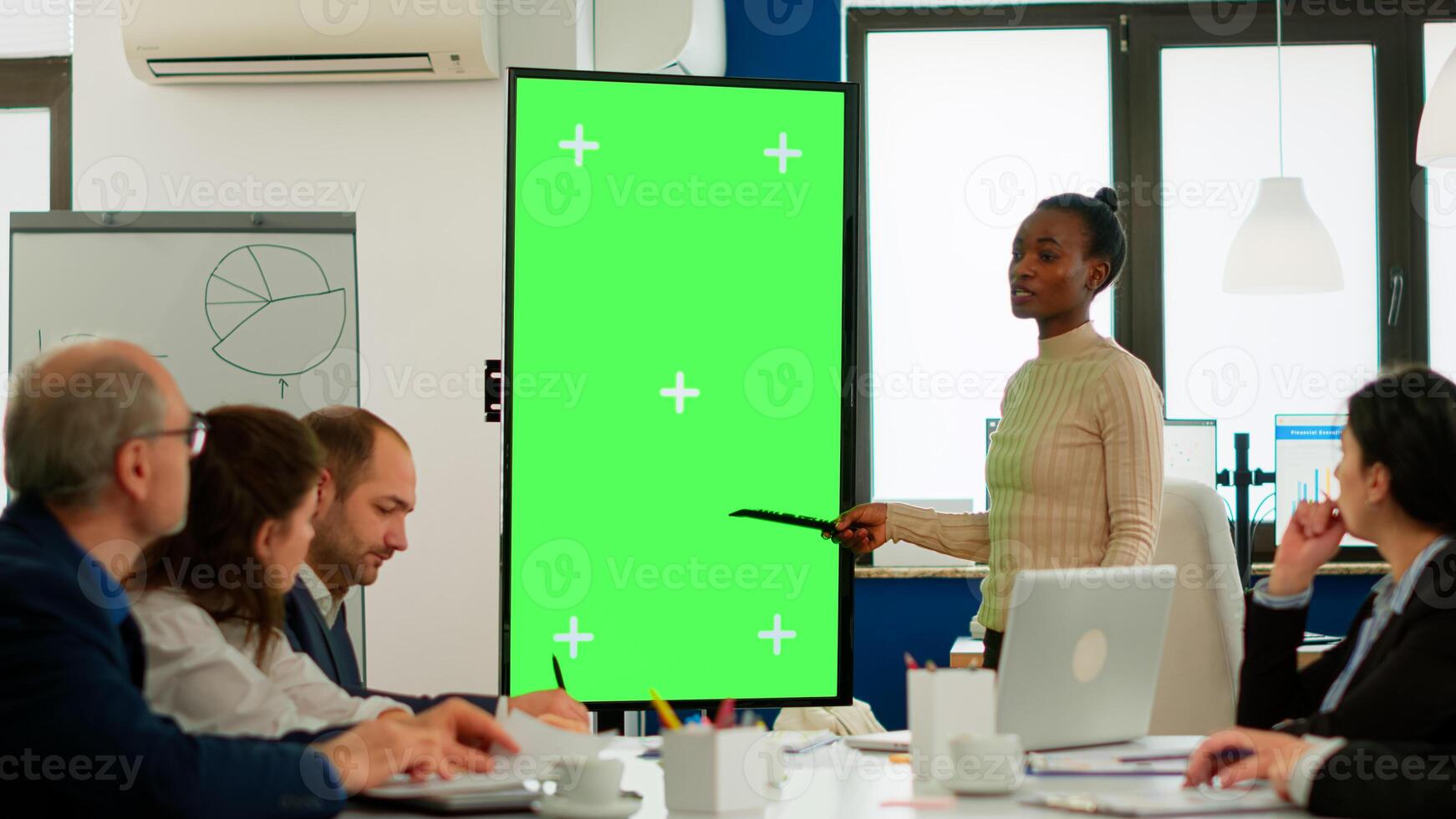 Diverse woman standing in start up office discussing strategy with green screen monitor in front of business partners. Manager explaining to multiethnic team project chroma key display mock up desktop photo