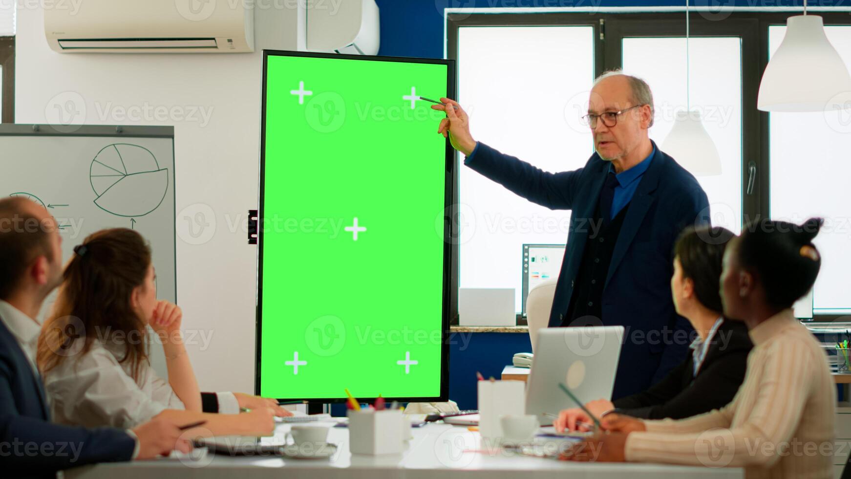 Mature businessman analysing annual financial reports standing in conference room pointing at green screen monitor. Leader explainig project strategy using mockup pc chroma key display in boardroom photo