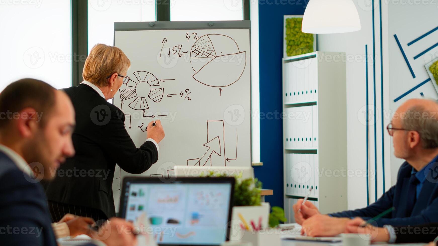 Senior business speaker woman presenting project writing on flip chart, answering question interacting with audience at corporate workshop, business coach and worker talking during conference training photo