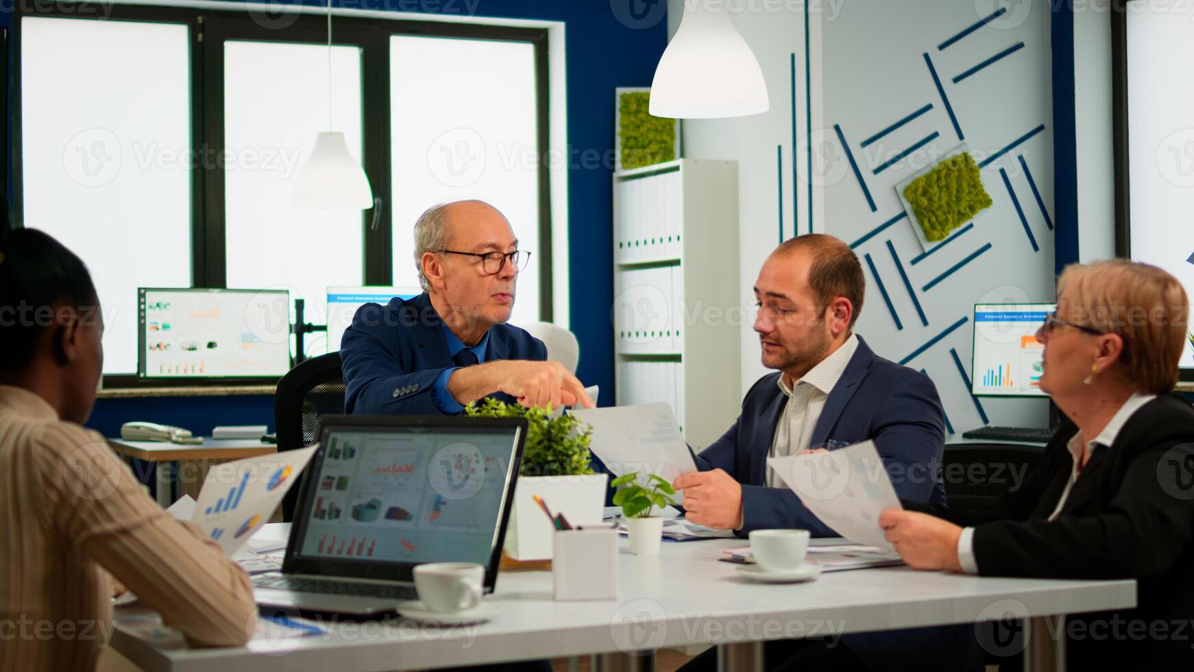 Senior businessman team leader brainstorming with colleague using paperwork showing ideas working in office. African woman using laptop in meeting broadroom, negotiations speaking with clients photo