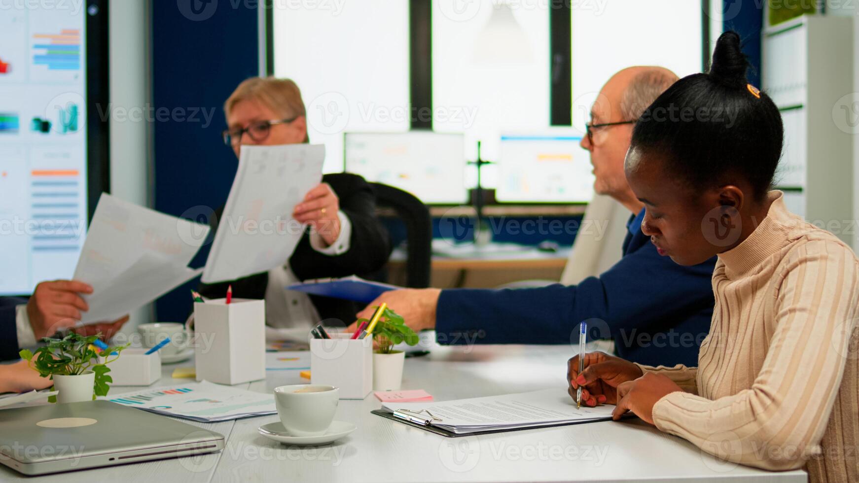 African businesswoman reading documents, signing its while business partners sharing paperwork sitting at conference table in broadroom. Executive director meeting shareholders in start up office photo