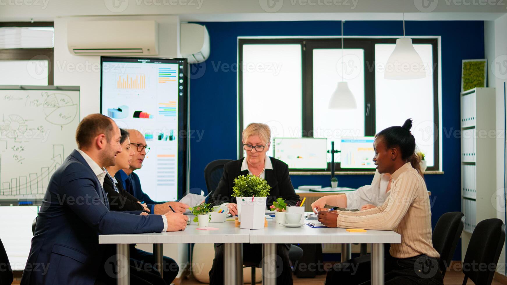 Business people comming in conference room ready for morning meeting. Mature project leader discussing with teamworkers in broadroom, analysing charts, graphs, financial evolution of company photo