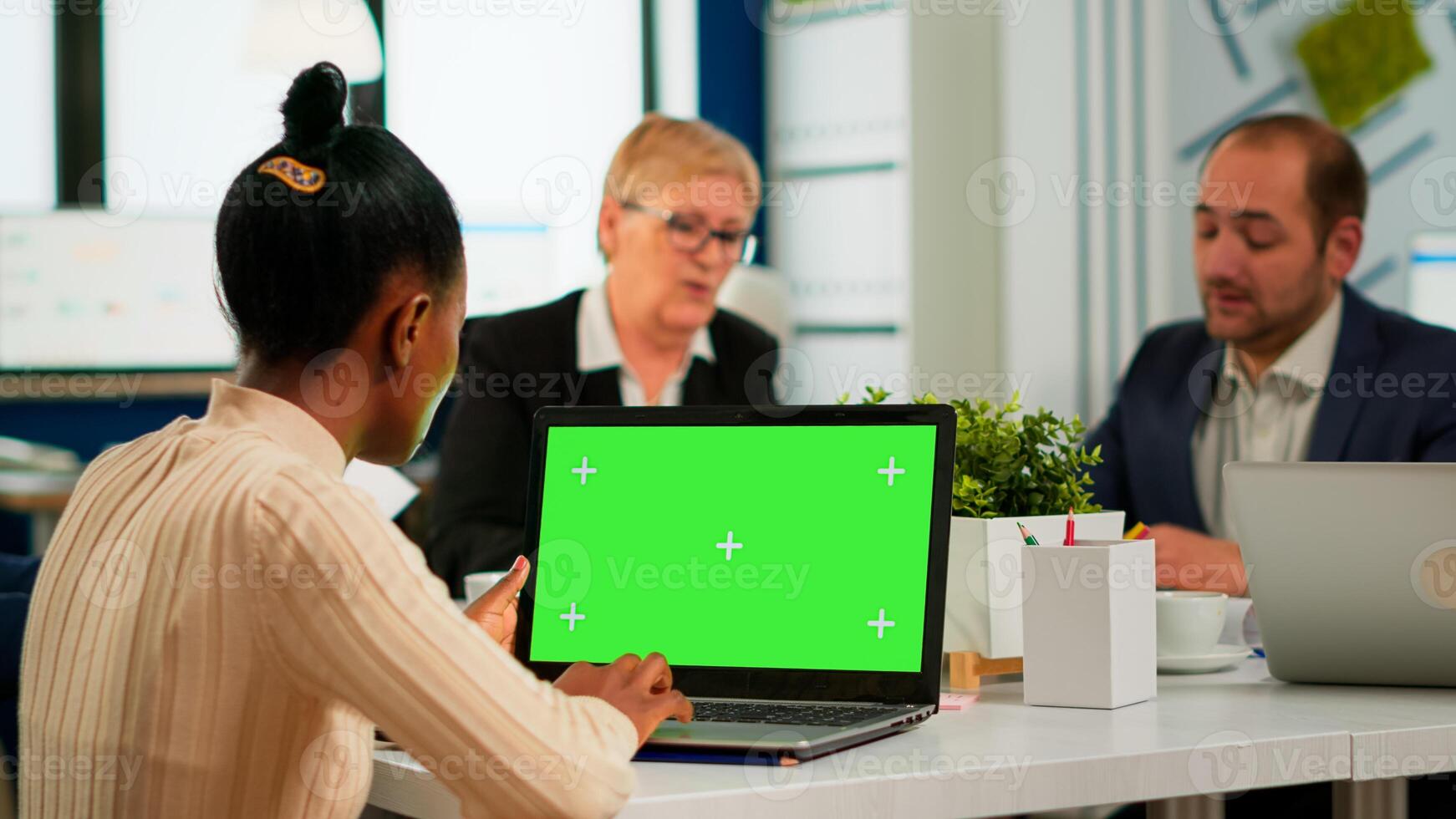 Over the sholder of african manager woman sitting at conference desk looking at laptop with green screen while diverse team working. Multiethnic people planning project on chroma key display photo