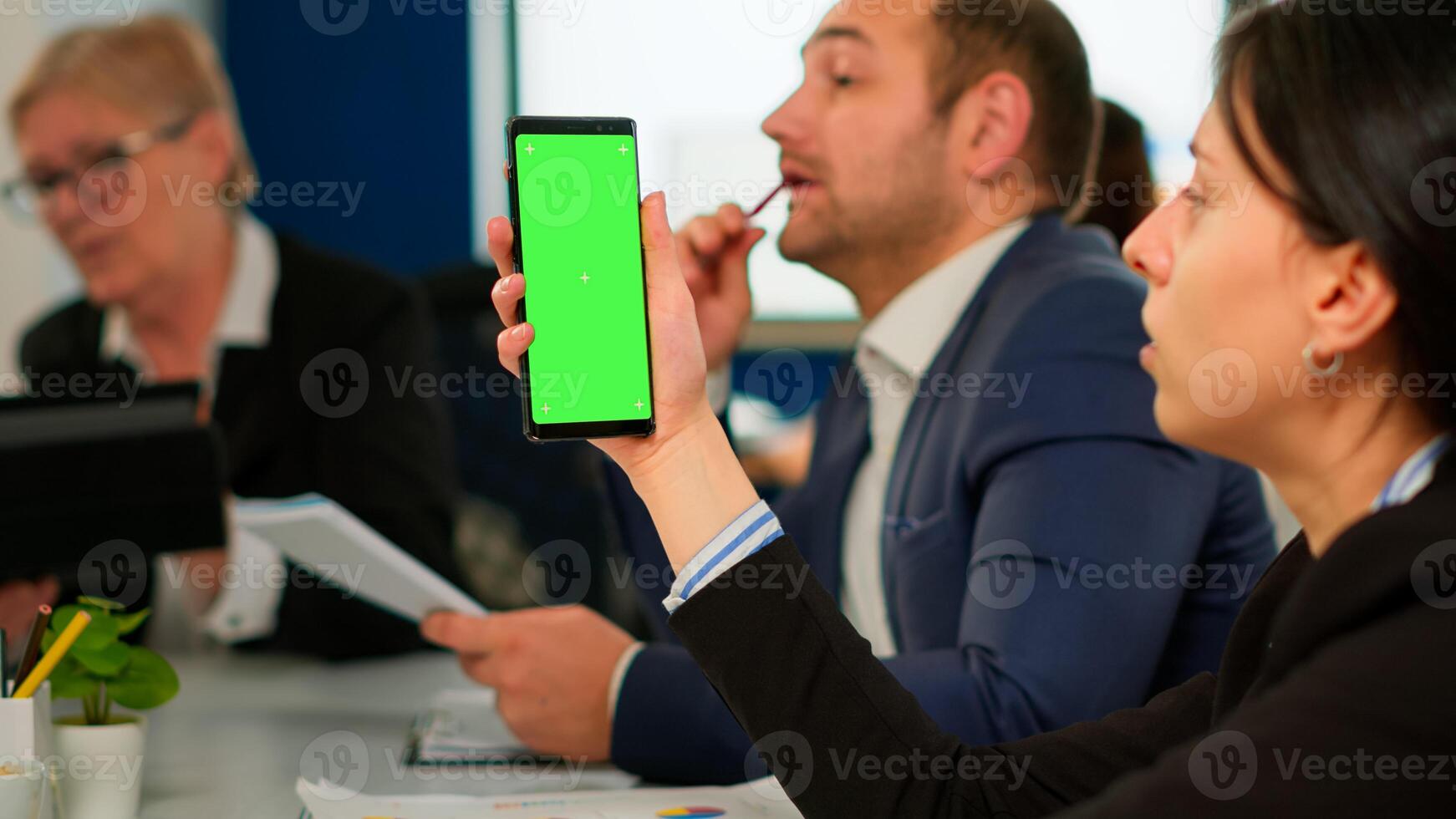 Businesspeople analysing annual financial reports sitting at desk while employee holding phone with green screen monitor. Leader explainig project strategy using greenscreen pc with chroma key display photo