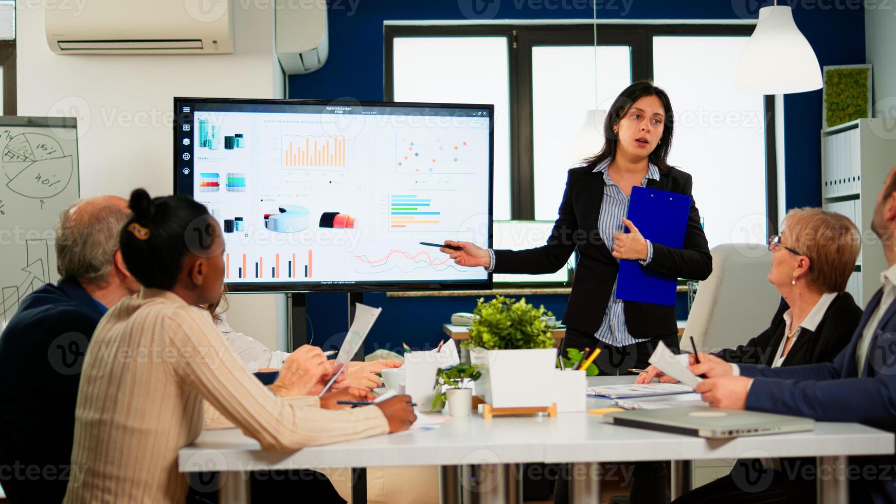 Female project manager holding financial meeting showing statistical graphs and charts on interactive whiteboard touchscreen device. Executive director working in broadroom of creative agency. photo