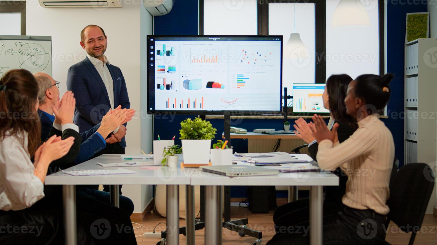 Succesful business man presenting the good evolution of company using digital interactive whiteboard with growth analysis, charts, statistics, data, Diverse people congratulate him clapping photo