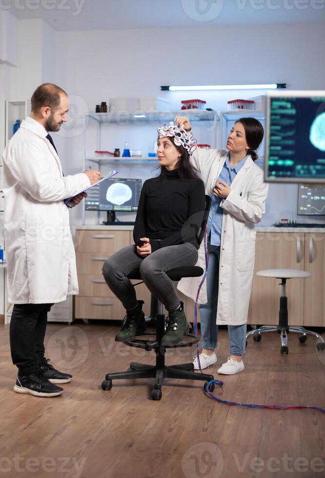 Professional neurological researcher explaning treatment result while medical scientist adjusting eeg headset preparing for brain scan analysing electrical activity, nervous system photo