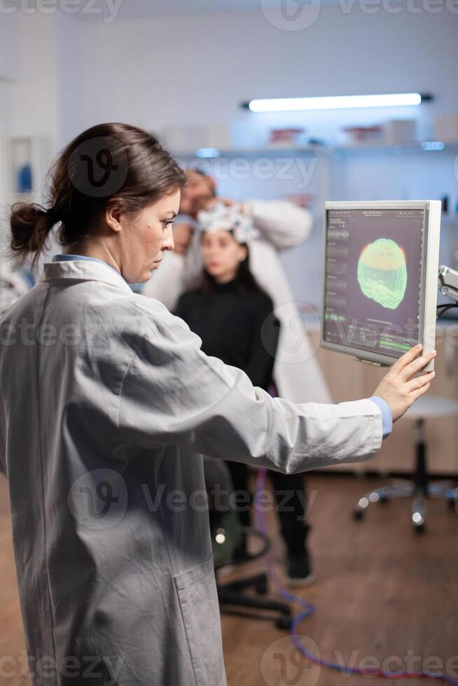 Neurology scientist examining brain nervous system scan on on monitor, machine with sensors attached to patient in laboratory. Medicine lab with modern digital machine. photo