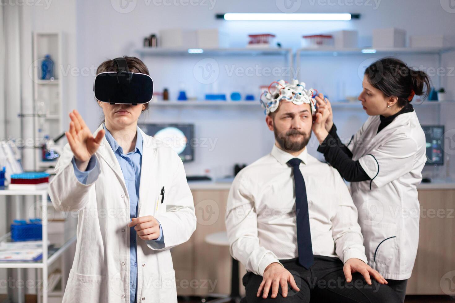 Neurologist doctor gesturing wearing virtual reality headset and assistant adjusting patient sensor that read brain activity , nervous system. Neuroscientist analysing diagnosis. photo