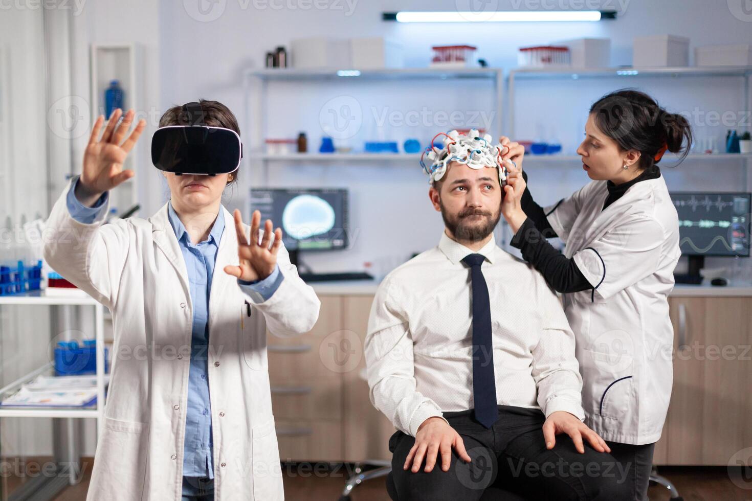 Neuroscientist developing diagnosis wearing virtual reality headset in medicine laboratory, assistant adjusting examining sensors on patient sitting on chair. Medicine lab with modern technology. photo