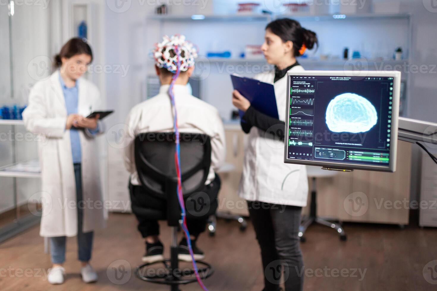 Man patient wearing performant eeg headset scanning brain electrical activity in neurological research laboratory while medical researcher controlling it, examining nervous system, nurse taking notes photo