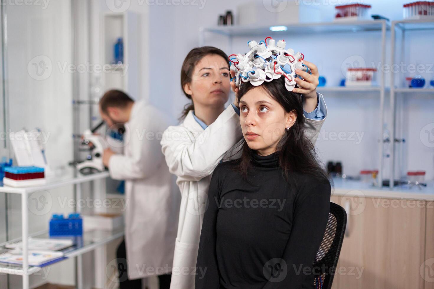 Woman wearing brain wave headset in modern medicine lab with neurologist doctor health physician. Neuroscience medic putting sensors on patient. Finding cure for disease. photo
