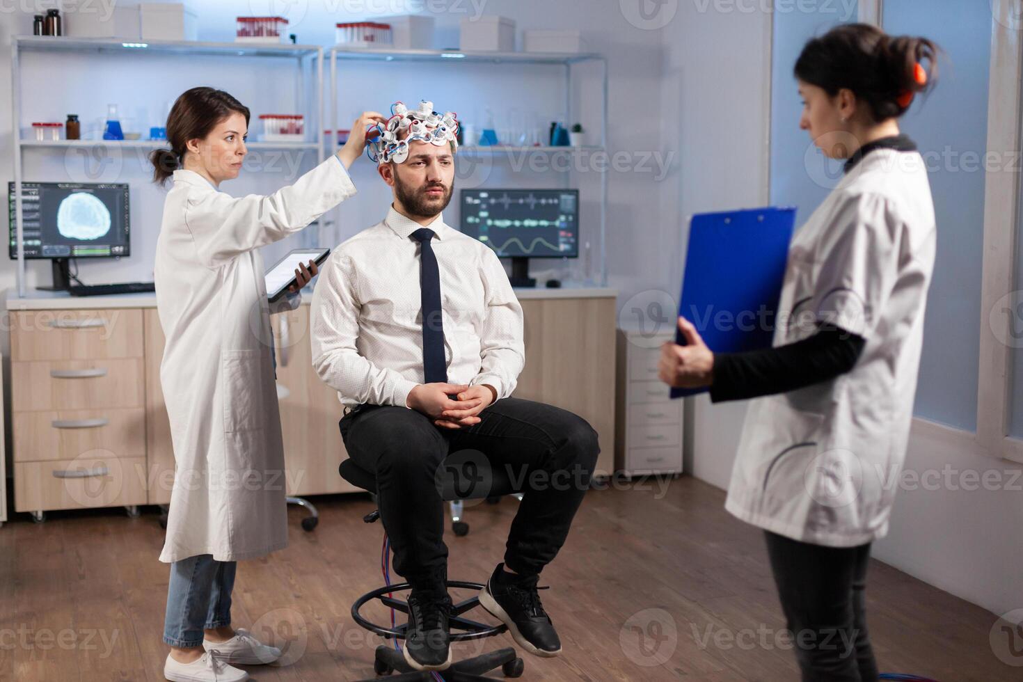 Ill man listening neurological doctor looking at clipboard wearing high tech headset scanning brain electrical activity. Patient sitting in scientific laboratory treating nervous system dysfunctions photo