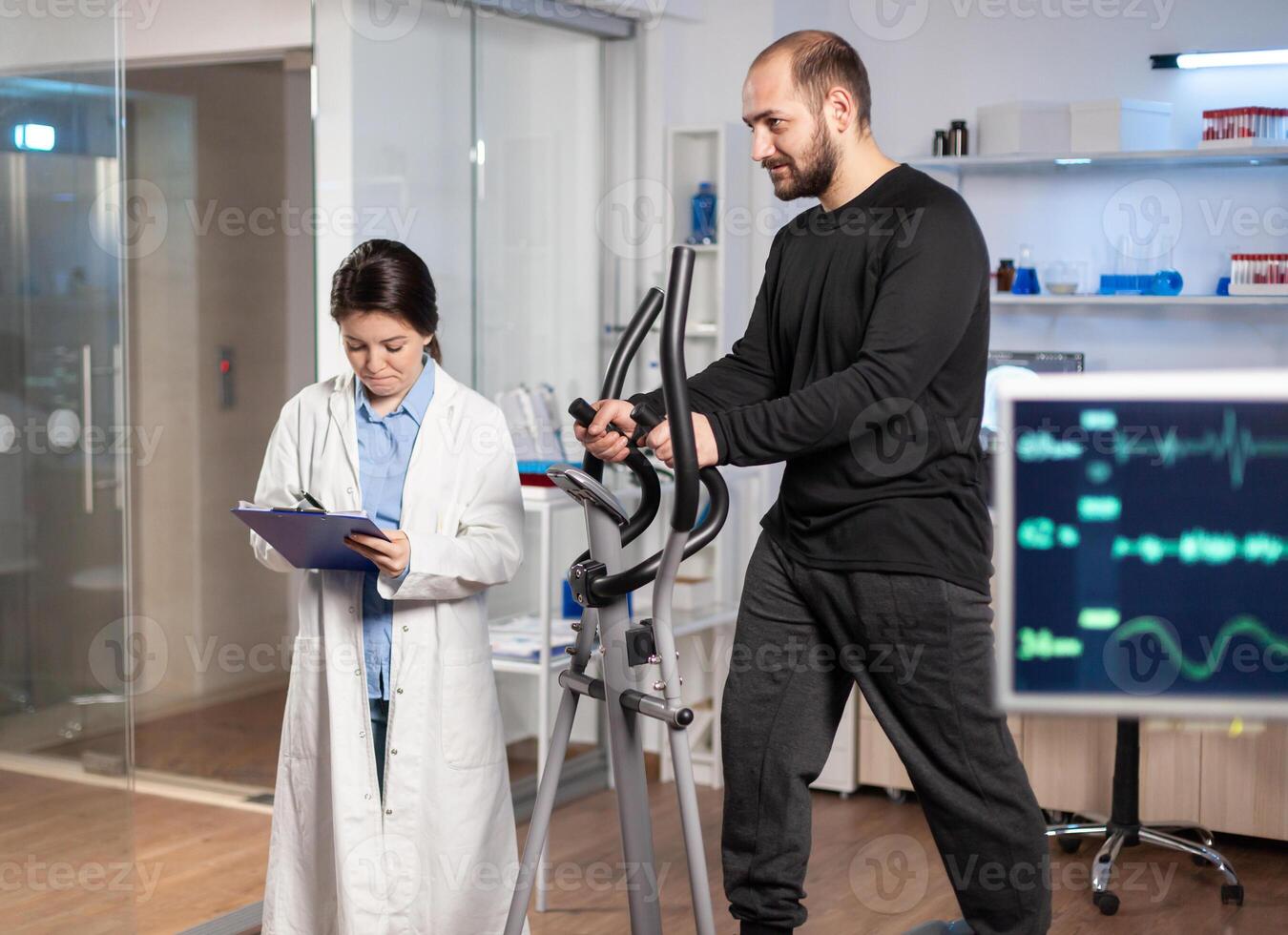 Sport researcher in laboratory taking notes while muscular athlete athlete is running, heart rate examination. Testing endurance in professional biomechanics lab. photo