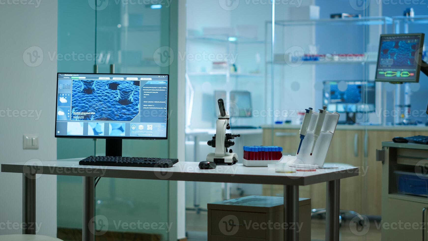 Modern empty biological applied science laboratory with technological microscopes, glass test tubes, micropipettes, desktop computers and displays. PC's are running sophisticated DNA calculations. photo