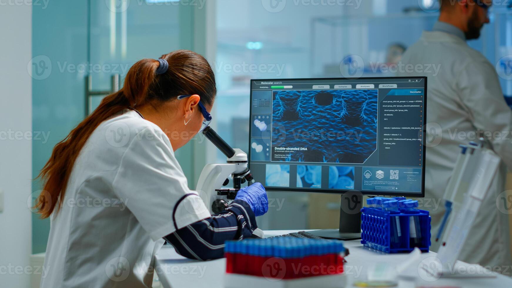 Biotechnology scientist researching in laboratory using microscope and typing on pc. Chemist examining virus evolution using high tech for scientific research of vaccine development against covid19 photo