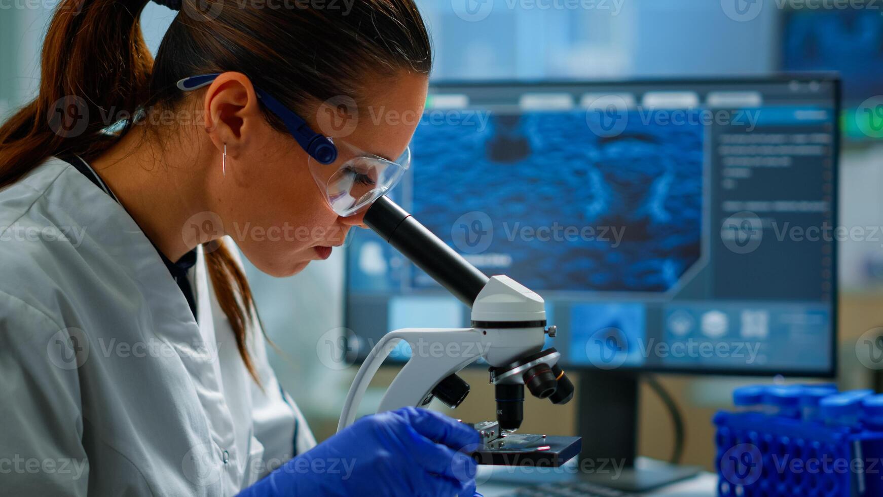 Portrait of scientist looking under microscope in medical development laboratory, analyzing petri dish sample. Medicine, biotechnology research in advanced pharma lab, examining virus evolution photo