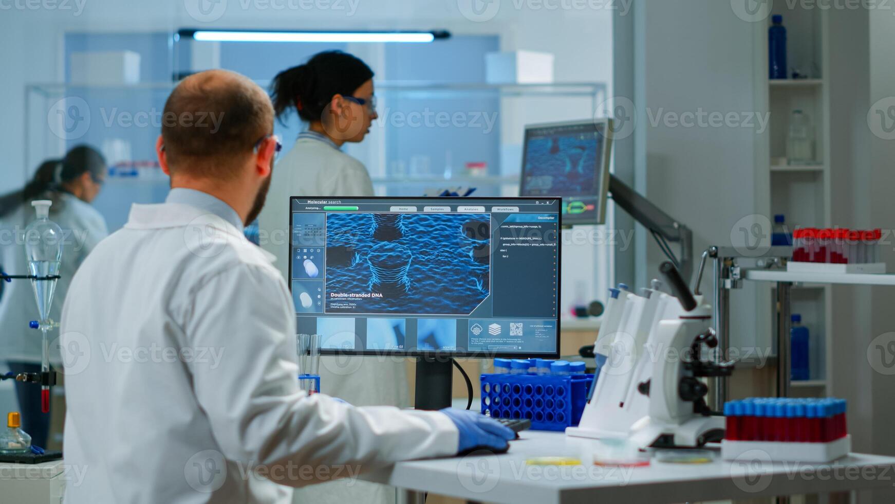 Man scientist working to develop a new vaccine in modern equipped laboratory, typing at computer. Group of biochemistry doctors examining virus evolution using high tech for researching treatment photo