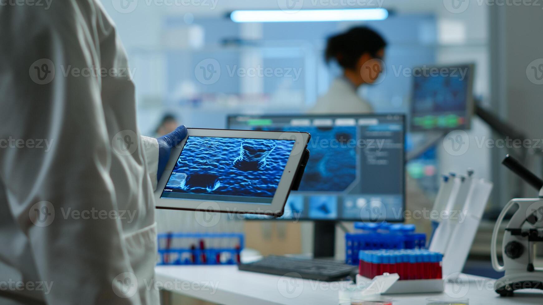 Close up of scientist in lab coat working holding tablet standing in modern equipped laboratory. Team chemists examining vaccine evolution using high tech and chemistry tools for virus development photo