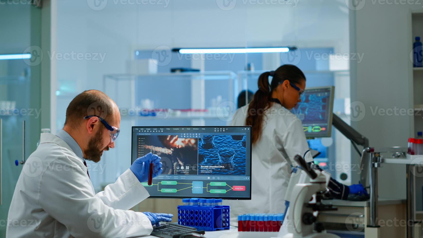 Laboratory medical stuff disscussing about vaccine development holding test tube with blood sample. Medical scientist working with DNA scan image in modern equipped laboratory using high tech photo