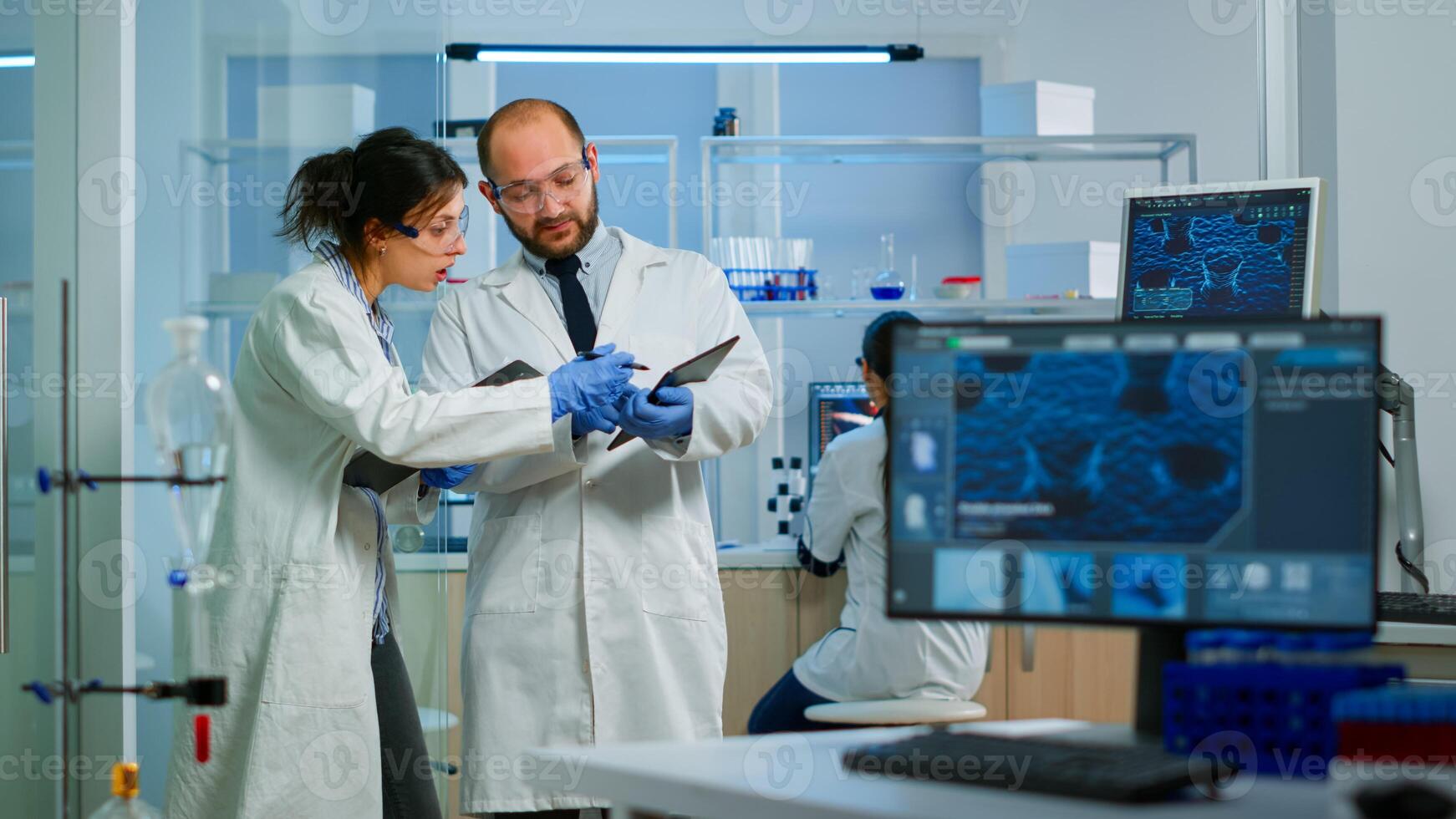 Scientists coworkers using digital tablet working in medical research laboratory, analysing biochemicals samples, talking. Scientific lab for medicine, microbiology development with advanced equipment photo