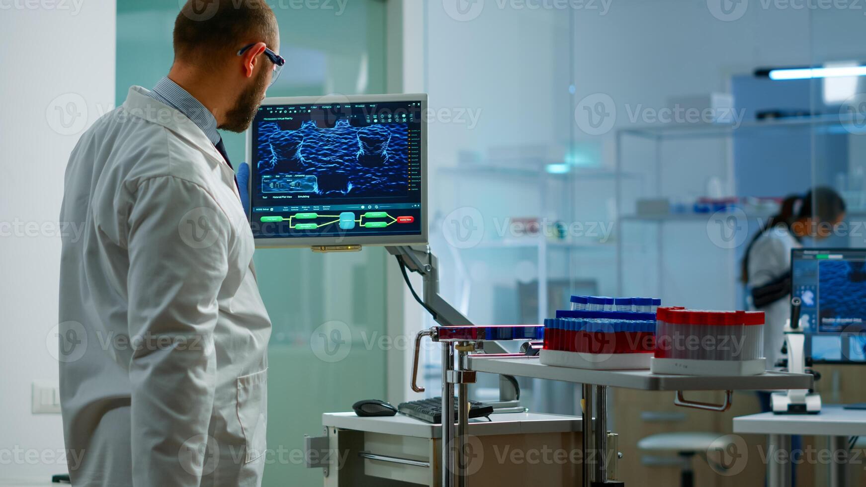 Scientist worried about virus evolution analysing DNA scan image standing in equipped laboratory typing at computer. Stuff examining vaccine development using high tech researching treatment photo