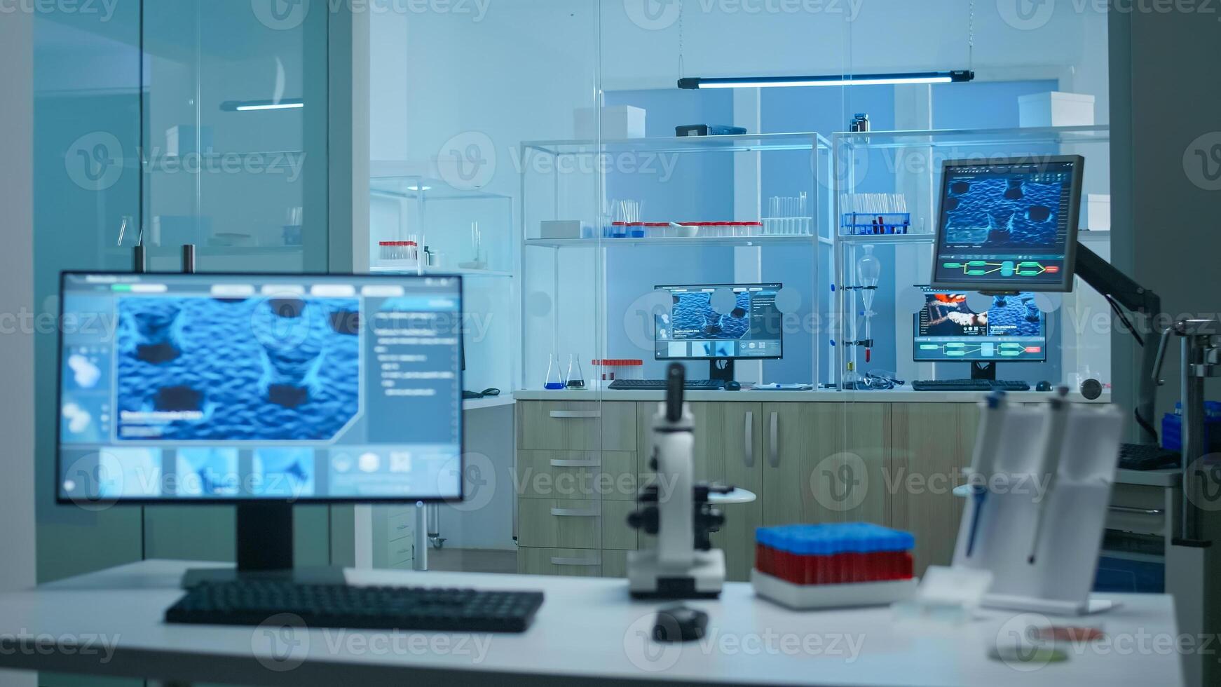 Modern empty research applied science laboratory with technological microscopes, glass test tubes, micropipettes, desktop computers and displays. PC's are running sophisticated DNA calculations. photo