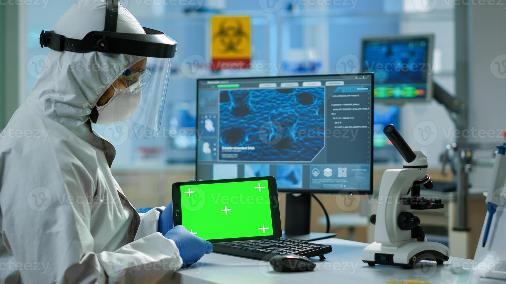 Doctor with coverall working at tablet with green screen in modern equipped lab. Team of microbiologists doing vaccine research writing on device with chroma key, isolated, mockup display. photo