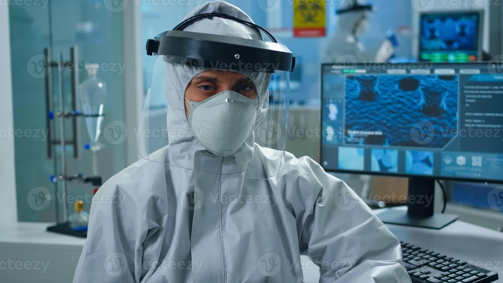 Overworked woman chemist sitting in modern equipped lab wearing coverall looking tired at camera. Team of doctors examining virus evolution using high tech and chemistry tools for vaccine development photo
