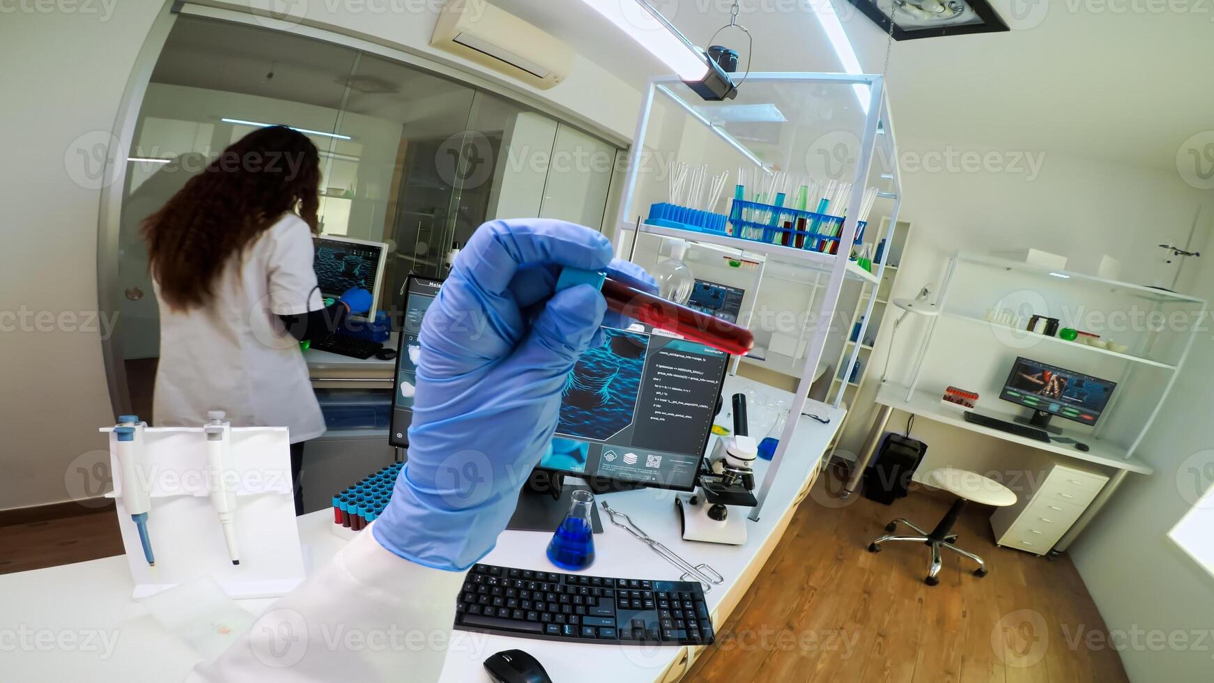 FPV of scientist holding blood sample from test tube analysing and typing on pc vaccine evolution. Team of doctors, viorolog researcher in professional lab working to discover medical treatment. photo