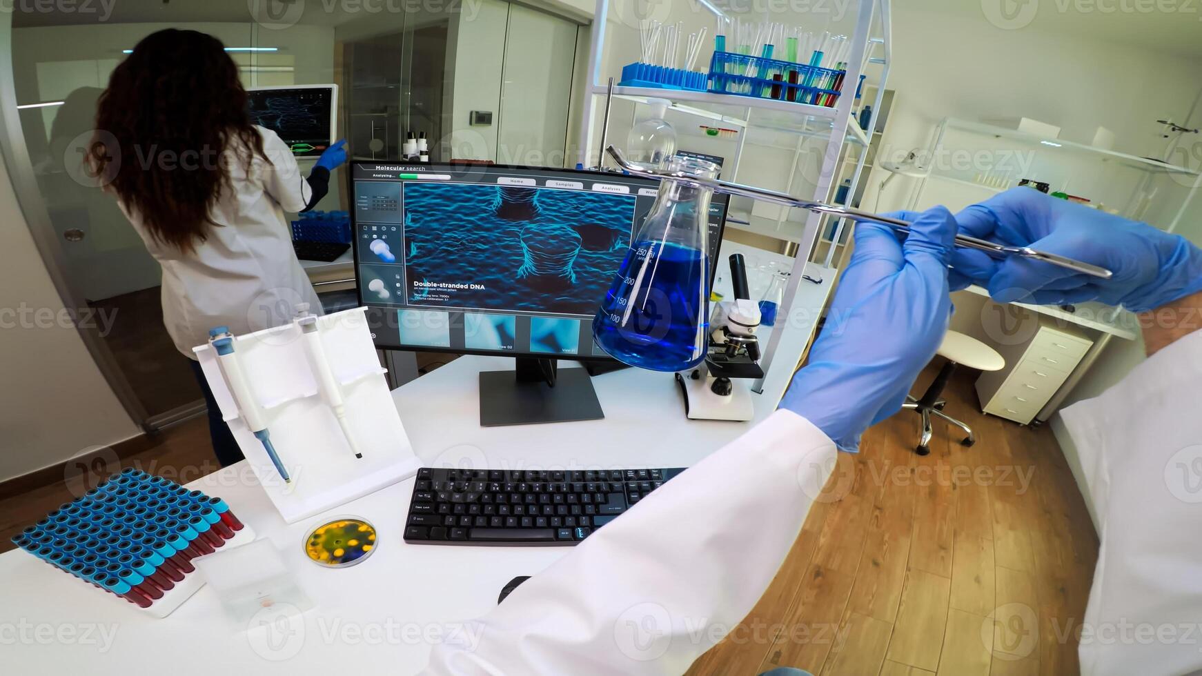 FPV of man researcher lifting chemical vessel with medical pliers, looking at blue sample. Scientists examining vaccine evolution in medical lab using high tech for scientific research. photo