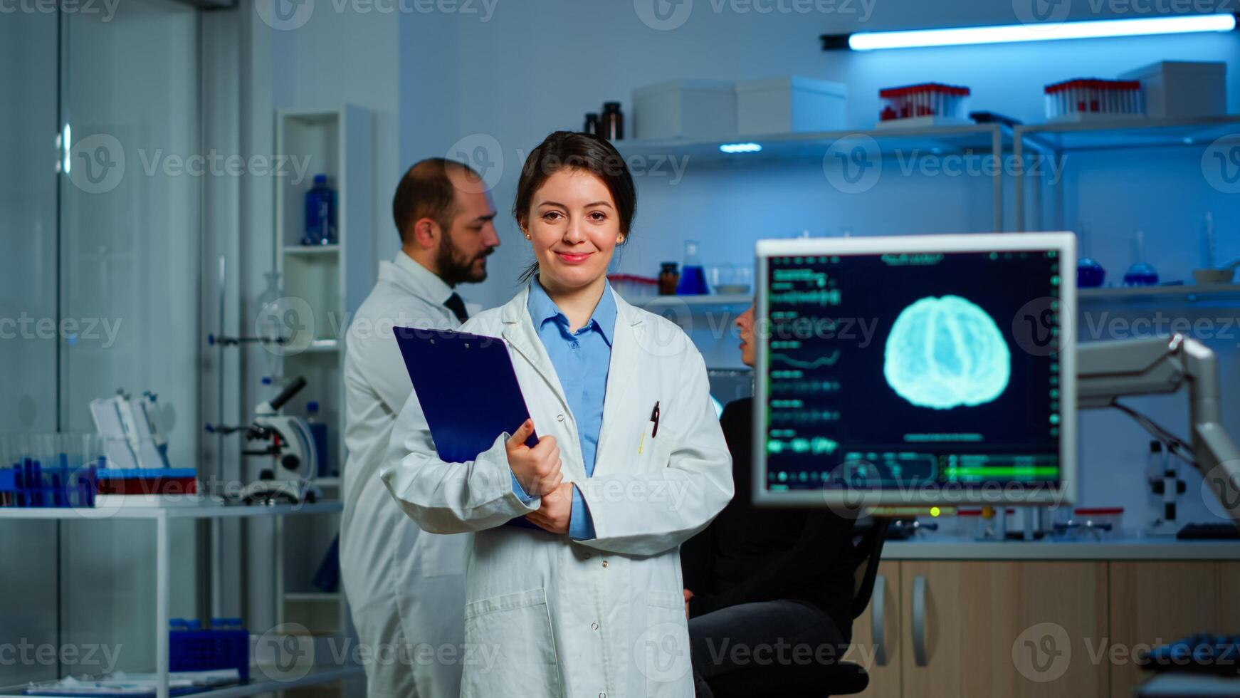 Portrait of scientist neurologist researcher looking at camera smiling while coworker discussing with patient in background about brain functions, nervous system, tomography scan working in laboratory photo