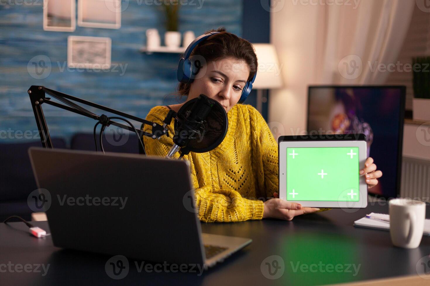 Influencer holding tablet with green screen and speaking into microphone during podcast in home studio. On-air production internet broadcast host streaming live content using chroma key mockup display. photo