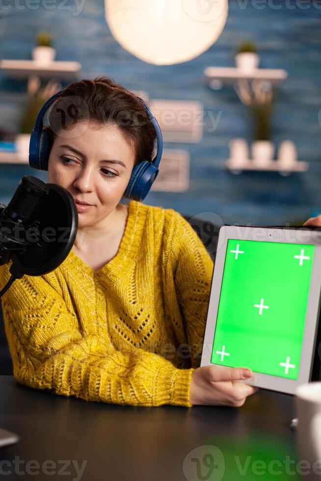 Vlogger looking at laptop and talking about tablet with chroma key desktop. On-air production internet broadcast host streaming live content using mochup, green screen, izolated desktop. photo