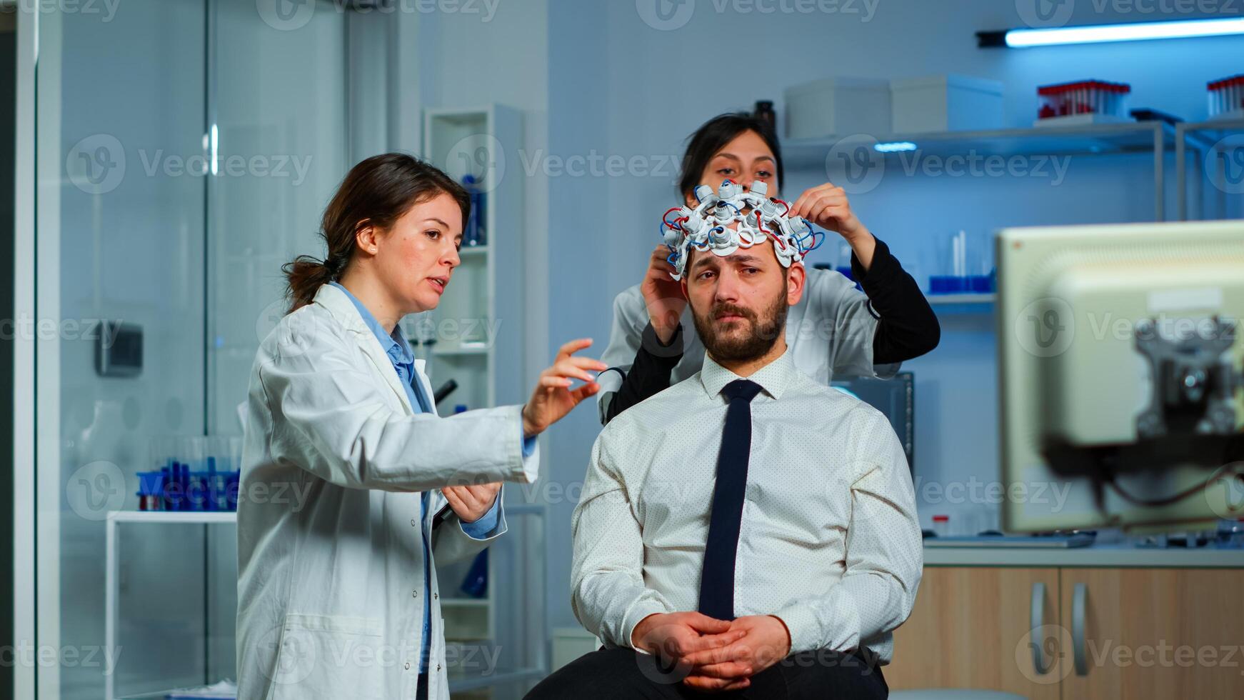 Neurological researchers explaning treatment result pointing on monitor while medical scientist adjusting brainwave scanning headset preparing for brain scan analysing electrical activity photo