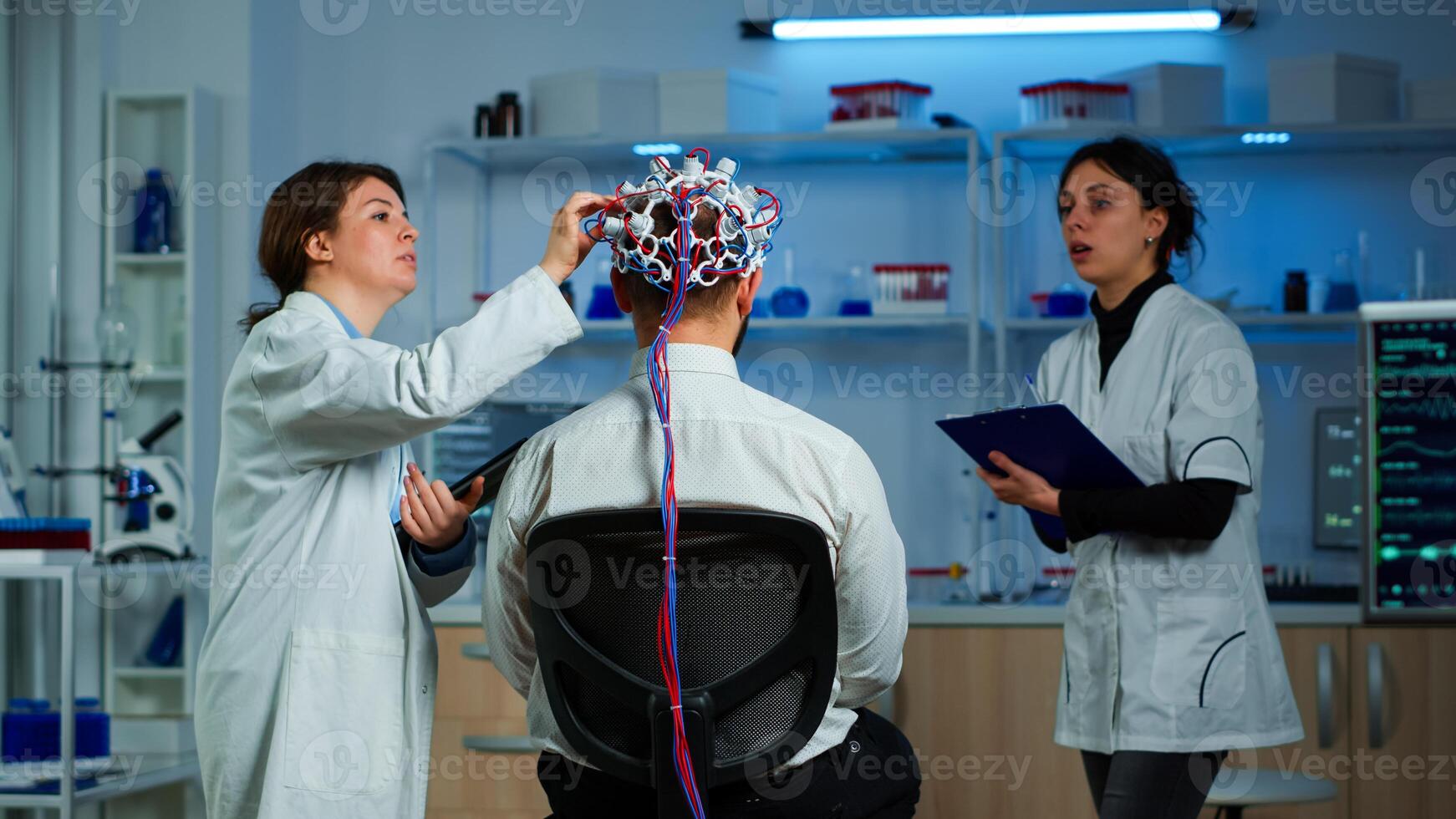 Man patient wearing performant eeg headset scanning brain electrical activity in neurological research laboratory while medical researcher controlling it, examining nervous system, nurse taking notes photo