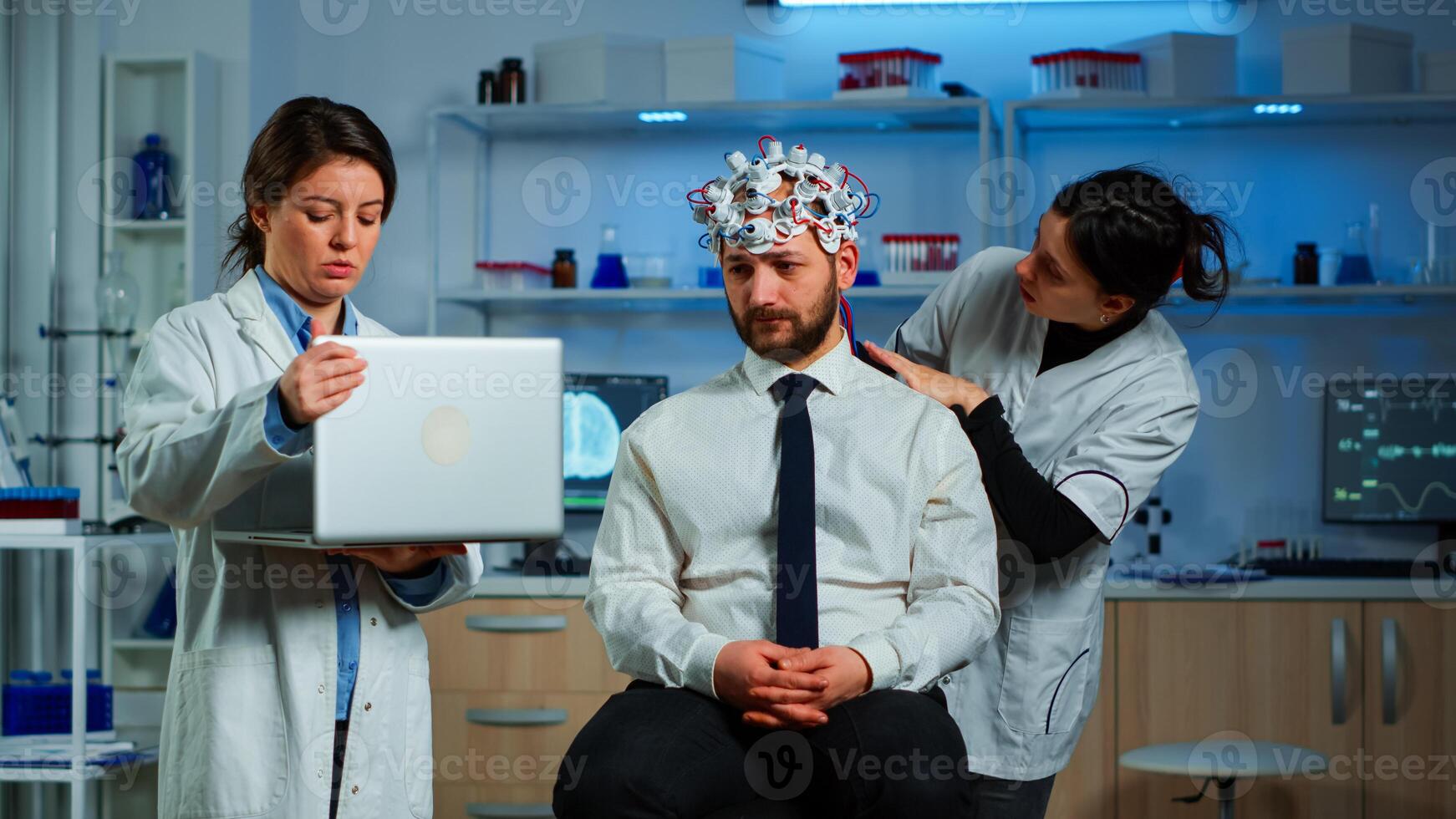 Medic in neuroscience working in neurological research laboratory developing brain experiment holding laptop explaning to man brainwave scanning headset side effects of nervous system treamtment. photo