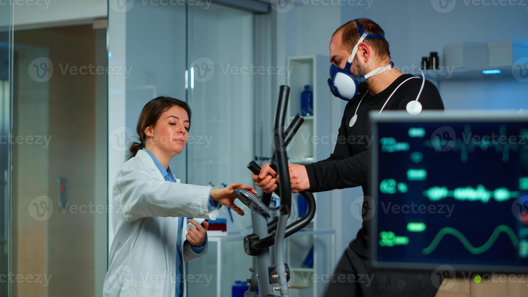 Specialist health supervisor increasing level of exercises monitoring endurance of athlete. Medical researcher measuring vo2 of performance sports running with mask on cross trainer in sport lab photo