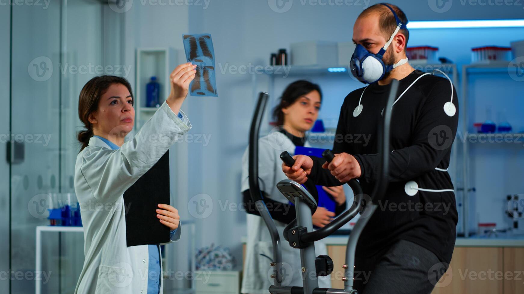Team of doctor researchers monitoring endurance of man performance sports wearing mask running cross trainer. Lab science doctor measuring vo2 of sportsman, looking at x-ray explaning health status photo