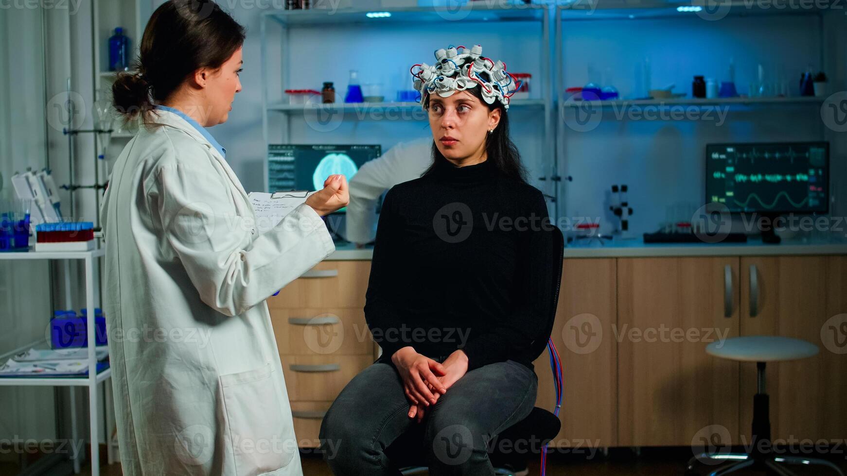 Professional neurological researcher in special medicine explaning treatment result holding clipboard after medical scientist adjusting eeg headset analysing health of nervous system in lab photo