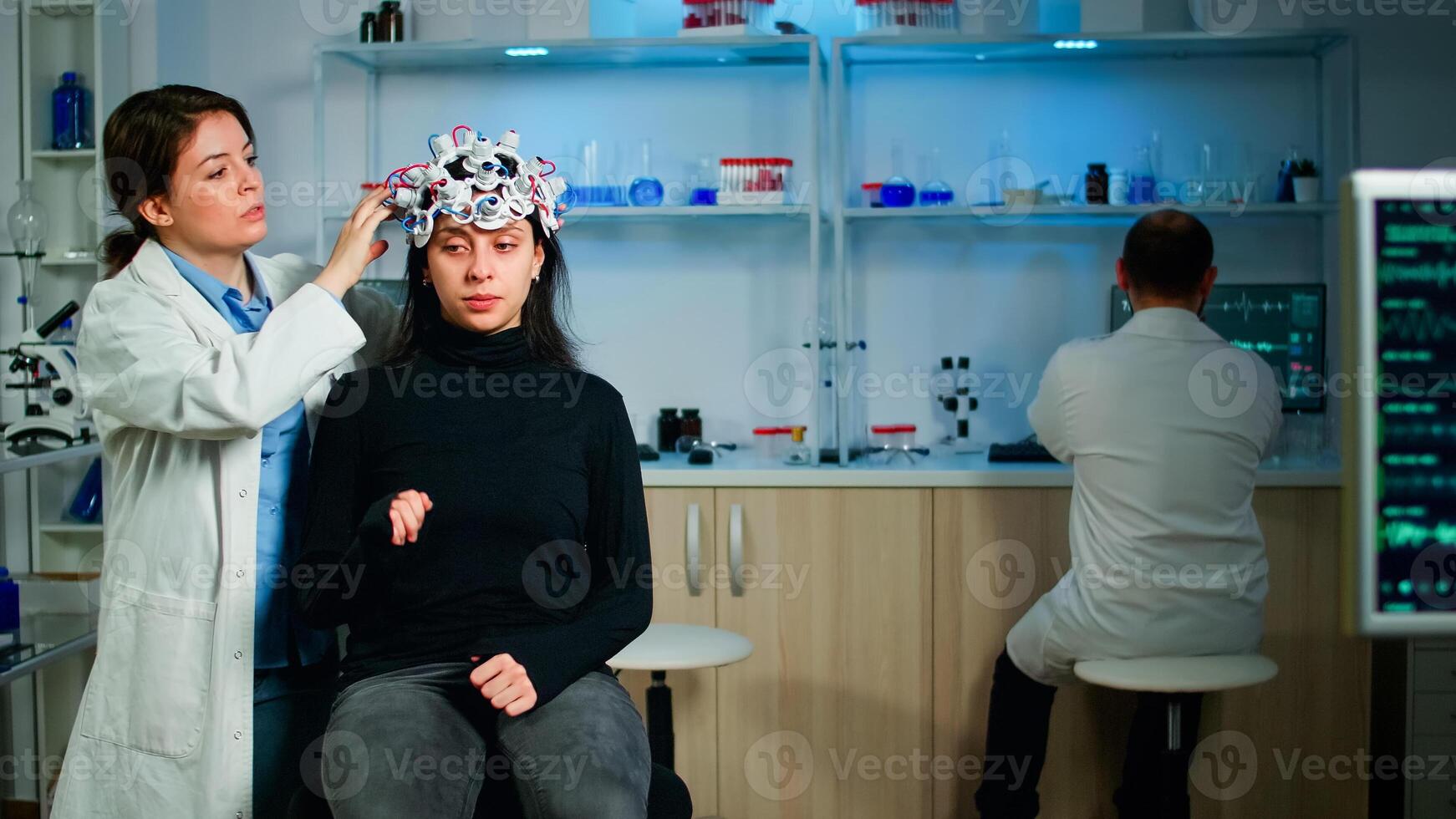 Medical lab technician adjusting eeg headset monitoring brain functions, descovering diagnosis of disease. Team of scientists researchers working late night in neurology clinic for woman health photo